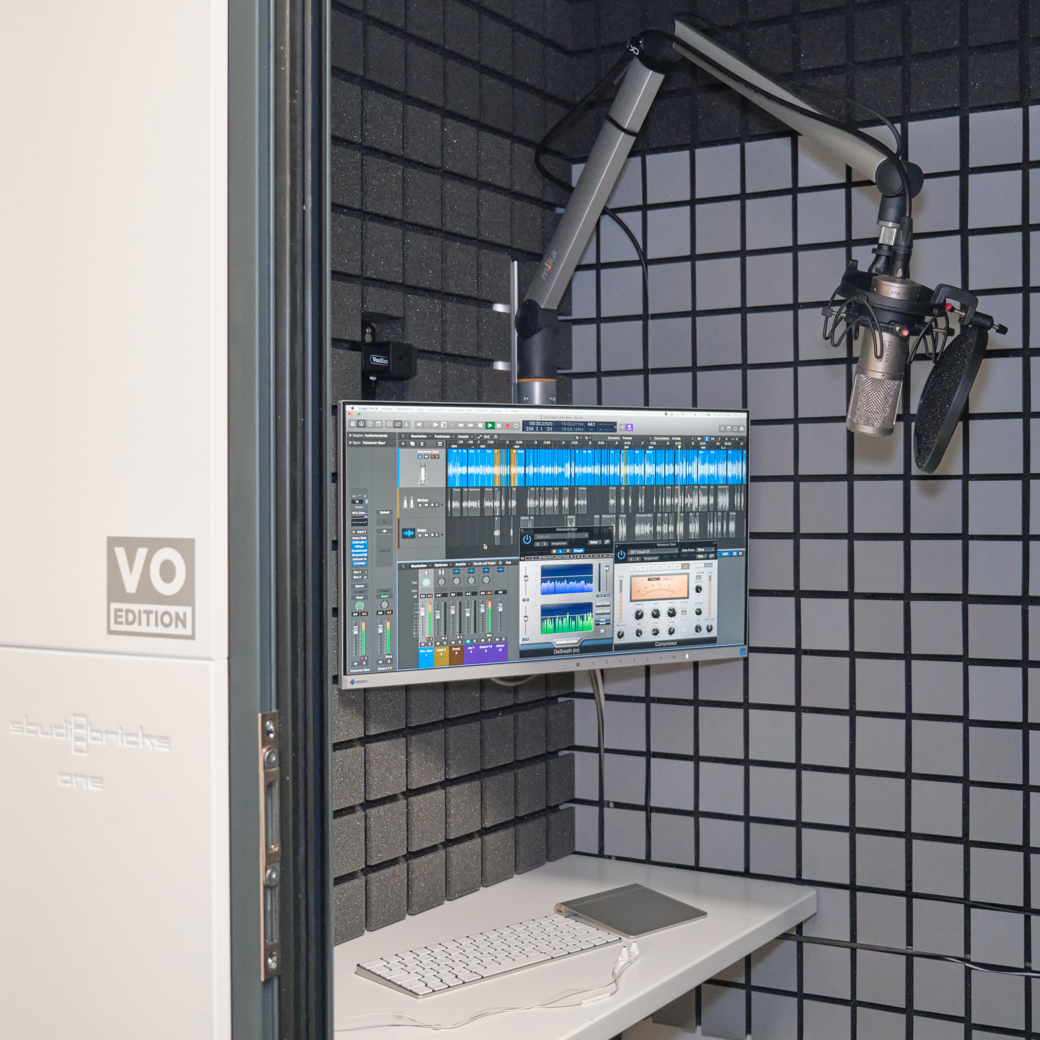 A look inside the recording booth: microphone on a boom arm, screen with editing software and keyboard